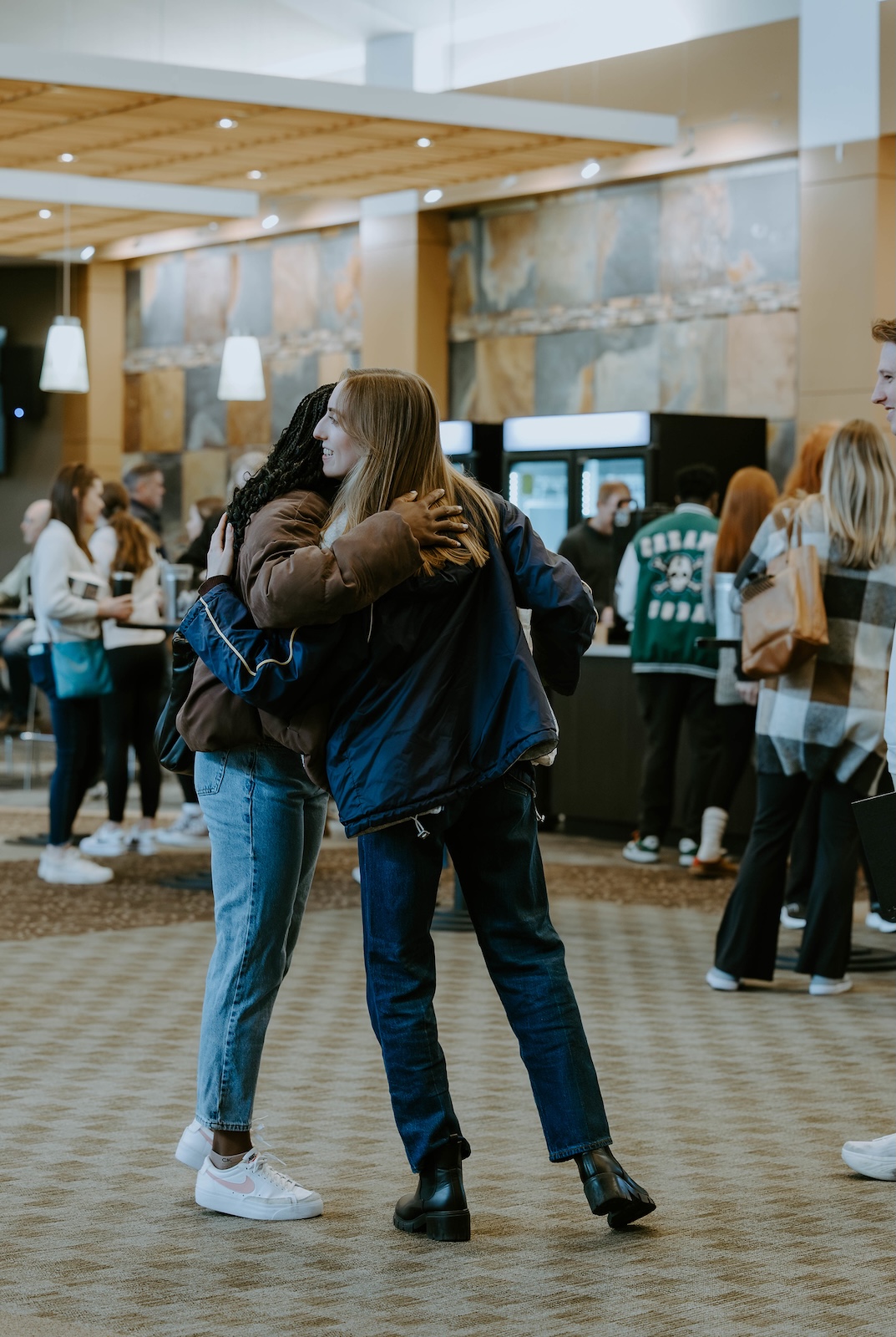 Two young women hugging each other inside a cafe area