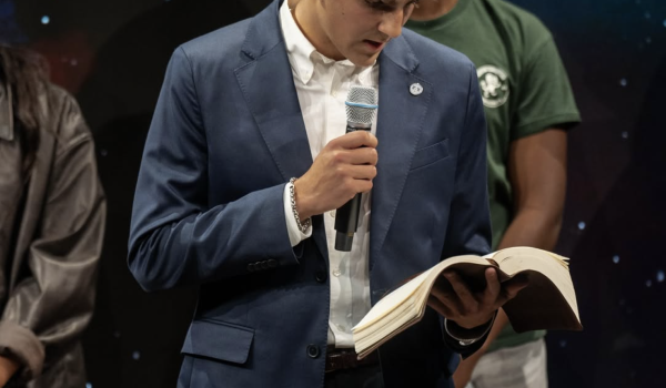 Man in a suit holding a microphone and reading from the Bible